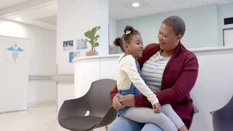 Glückliche-Afroamerikanische-Mutter,-Die-Tochter-Auf-Knien-Im-Wartezimmer-Des-Krankenhauses-Hält,-Zeitlupe