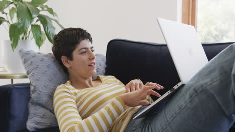 Glückliche-Kaukasische-Frau,-Die-Auf-Dem-Sofa-Liegt,-Einen-Laptop-Benutzt-Und-In-Einem-Sonnigen-Haus-Lächelt