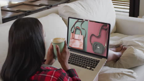 Biracial-woman-on-couch-with-coffee,-using-laptop-for-online-shopping,-slow-motion