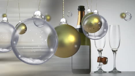 Swinging-gold-and-clear-christmas-baubles-over-champagen-bottle-and-glasses-on-grey-background
