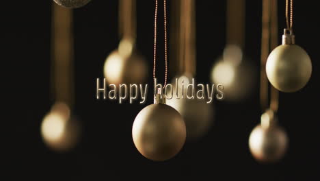 Happy-holidays-text-with-silver-christmas-baubles-hanging-on-dark-background