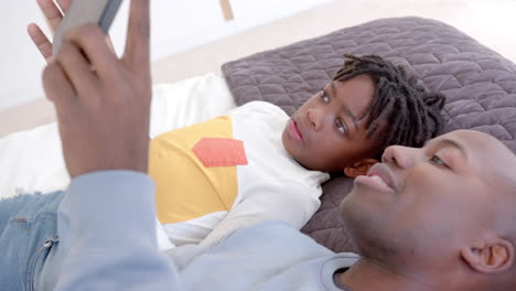 Feliz-Padre-E-Hijo-Afroamericanos-Acostados-En-La-Cama-Usando-Una-Tableta-En-Casa,-Cámara-Lenta
