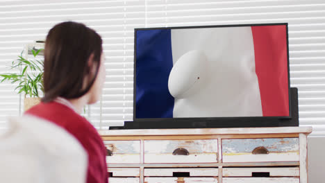 Caucasian-woman-watching-tv-with-rugby-ball-on-flag-of-france-on-screen