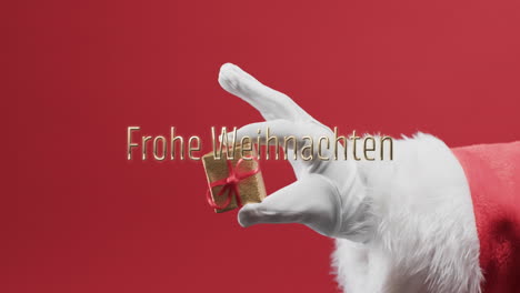 Frohe-Weihnachten-Texto-Sobre-La-Mano-De-Papá-Noel-Sosteniendo-Un-Pequeño-Regalo-Sobre-Fondo-Rojo