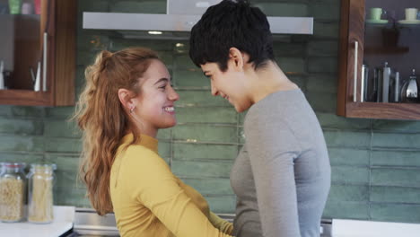 Happy-caucasian-lesbian-couple-embracing-and-dancing-in-sunny-kitchen