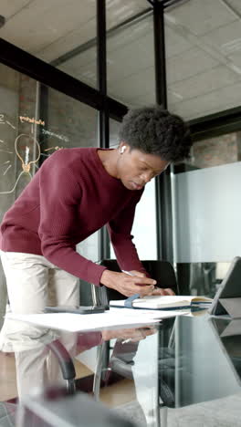 Video-Vertical-De-Un-Hombre-Afroamericano-Usando-Tableta-Y-Tomando-Notas-En-Casa,-Cámara-Lenta