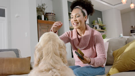 Mujer-Birracial-Acariciando-A-Un-Perro-Golden-Retriever-Usando-Un-Teléfono-Inteligente-Y-Una-Tarjeta-De-Crédito-En-Casa,-Cámara-Lenta