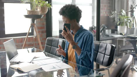 African-american-casual-businessman-sitting-at-desk-talking-on-smartphone-at-home,-slow-motion