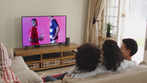 Biracial-family-watching-tv-with-diverse-male-rugby-players-with-ball-on-screen