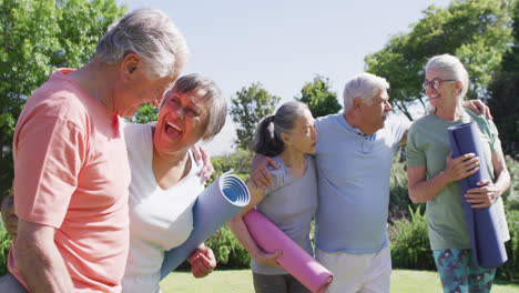 Diverse-group-of-happy-male-and-female-seniors-talking-after-exercising-in-sunny-garden,-slow-motion