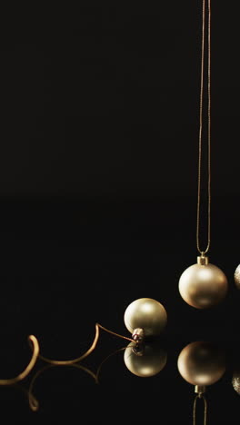 Vertical-video-of-gold-baubles-christmas-decorations-and-copy-space-on-black-background
