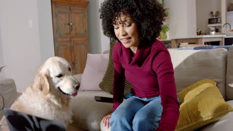 Happy-biracial-woman-with-golden-retriever-dog-using-laptop-at-home,-slow-motion