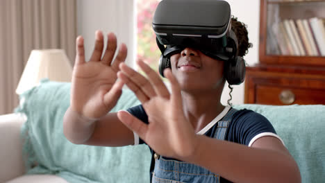 African-american-girl-using-vr-headset-and-touching-virtual-screen-in-living-room,-slow-motion
