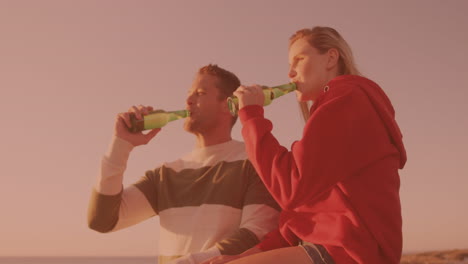 Kaukasisches-Paar,-Das-Zusammen-Am-Strand-Anstößt-Und-Bier-Trinkt
