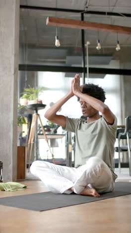 Video-Vertical-De-Un-Hombre-Afroamericano-Haciendo-Yoga-Y-Meditando-En-Casa,-Cámara-Lenta