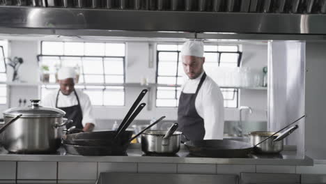 Dos-Chefs-Varones-Diversos-Preparando-Comidas-En-La-Cocina,-Cámara-Lenta