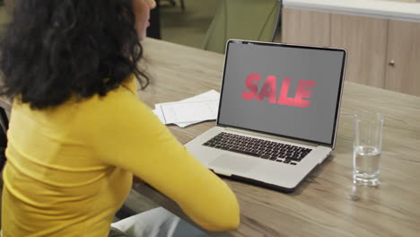 Biracial-woman-at-table-using-laptop,-online-shopping-during-sale,-slow-motion