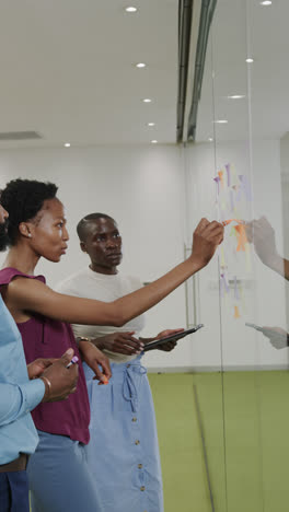 Vertical-video-of-african-american-business-people-taking-notes-on-glass-wall-in-slow-motion