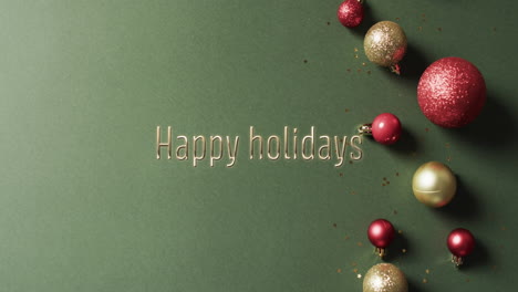 Happy-holidays-text-with-glittery-christmas-baubles-on-green-background