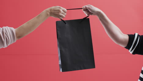 Video-of-hands-of-caucasian-women-holding-black-shopping-bag-with-copy-space-on-red-background