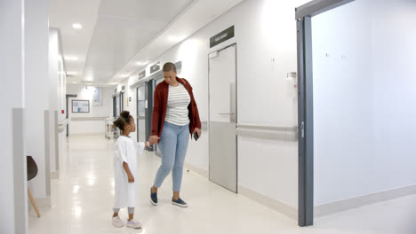 African-american-mother-and-daughter-in-hospital-gown-holding-hands-walking-in-corridor,-slow-motion