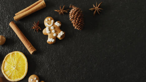Video-of-smiling-gingerbread-men-and-spices,-slices-of-orange-and-nuts-over-black-background