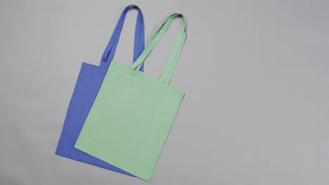 Close-up-of-blue-and-green-bags-on-grey-background,-with-copy-space,-slow-motion