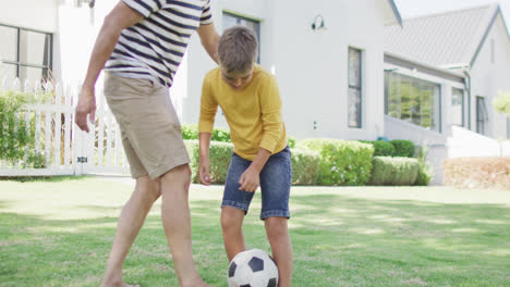 Glücklicher-Kaukasischer-Großvater-Und-Enkel-Spielen-Fußball-Im-Garten,-Zeitlupe