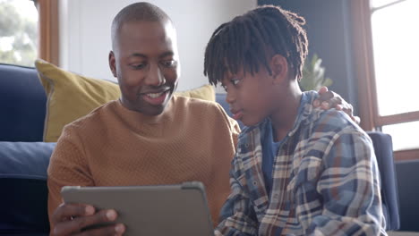 Happy-african-american-father-and-son-sitting-on-floor-and-using-tablet-at-home,-slow-motion