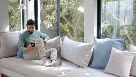 Biracial-man-sitting-on-sofa-using-smartphone-for-online-shopping-at-home,-slow-motion