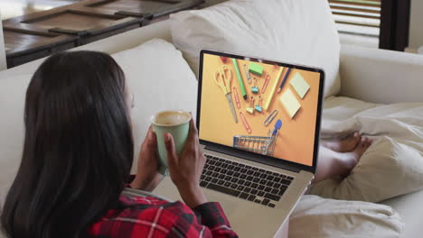 Biracial-woman-using-laptop-on-couch-at-home-online-shopping-for-stationery,-slow-motion