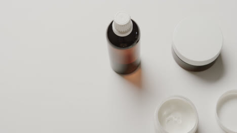 Close-up-of-cream-tubs-and-glass-bottle-with-copy-space-on-white-background-with-copy-space