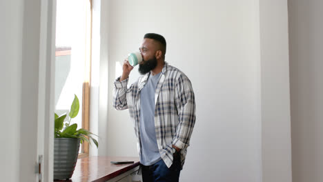 Afroamerikanischer-Mann-Trinkt-Kaffee-Und-Schaut-Zu-Hause-Aus-Dem-Fenster,-Zeitlupe