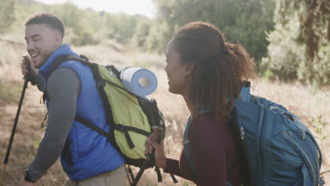 Happy-african-american-couple-hiking-with-trekking-poles-in-forest,-slow-motion