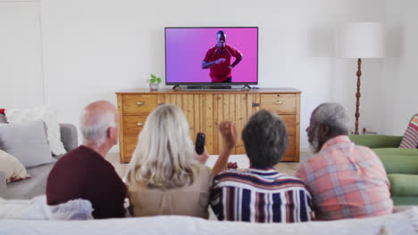 Senior-diverse-friends-watching-tv-with-african-american-male-rugby-player-catching-ball-on-screen