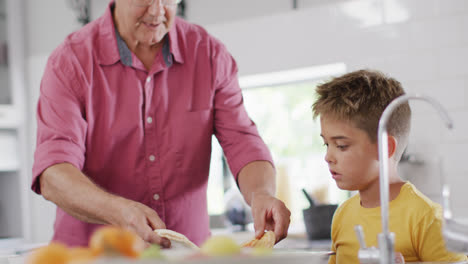 Happy-caucasian-grandfather-and-grandson-making-pizza-in-kitchen,-slow-motion