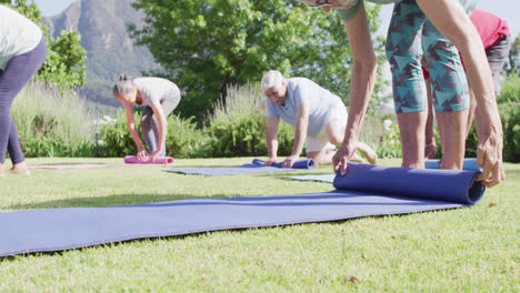 Diverse-group-of-male-and-female-seniors-rolling-up-yoga-mats-after-exercise-in-garden,-slow-motion