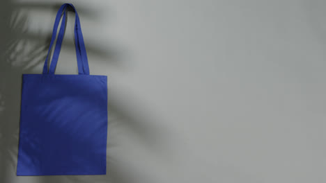 Blattschatten-Bewegt-Sich-über-Blaue-Tasche-Auf-Grauem-Hintergrund,-Kopierraum,-Zeitlupe