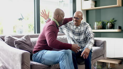 Happy-african-american-senior-father-and-son-sitting-on-couch,embracing-and-laughing,-slow-motion