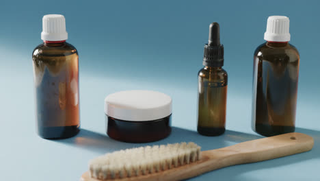 Close-up-of-glass-bottles,-cream-tub-and-brush-with-copy-space-on-blue-background