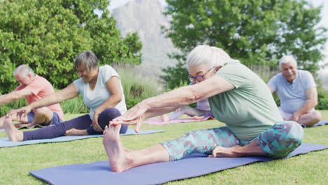 Diverse-group-of-happy-male-and-female-seniors-stretching-on-yoga-mats-in-sunny-garden,-slow-motion