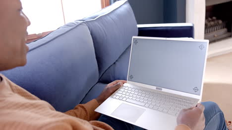 Happy-african-american-man-sitting-on-sofa-using-laptop-with-copy-space-at-home,-slow-motion
