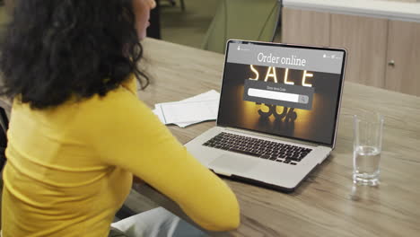 Biracial-woman-at-table-using-laptop,-online-shopping-during-sale,-slow-motion