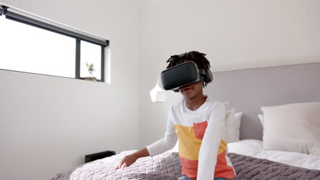 African-american-boy-sitting-on-bed-using-vr-headset-at-home,-slow-motion
