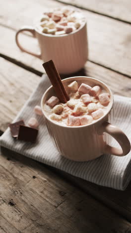 Vertical-video-of-mugs-of-chocolate,-marshmallows,-decorations-and-copy-space-on-wooden-background