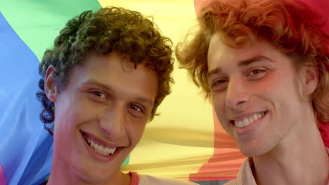 Portrait-of-happy-diverse-gay-male-couple-holding-rainbow-lgbt-flag-and-smiling,-slow-motion
