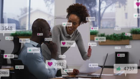 Animation-of-social-media-icons-falling-against-african-american-man-and-woman-discussing-at-office