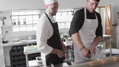 Focused-caucasian-male-chef-instructing-trainee-male-chef-in-kitchen,-slow-motion
