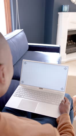 Vertical-video-of-african-american-man-using-laptop-with-copy-space-on-screen-at-home,-slow-motion