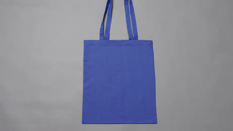 Close-up-of-blue-bag-on-grey-background,-with-copy-space,-slow-motion